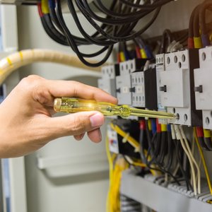 Electricians hands testing current electric in control panel.